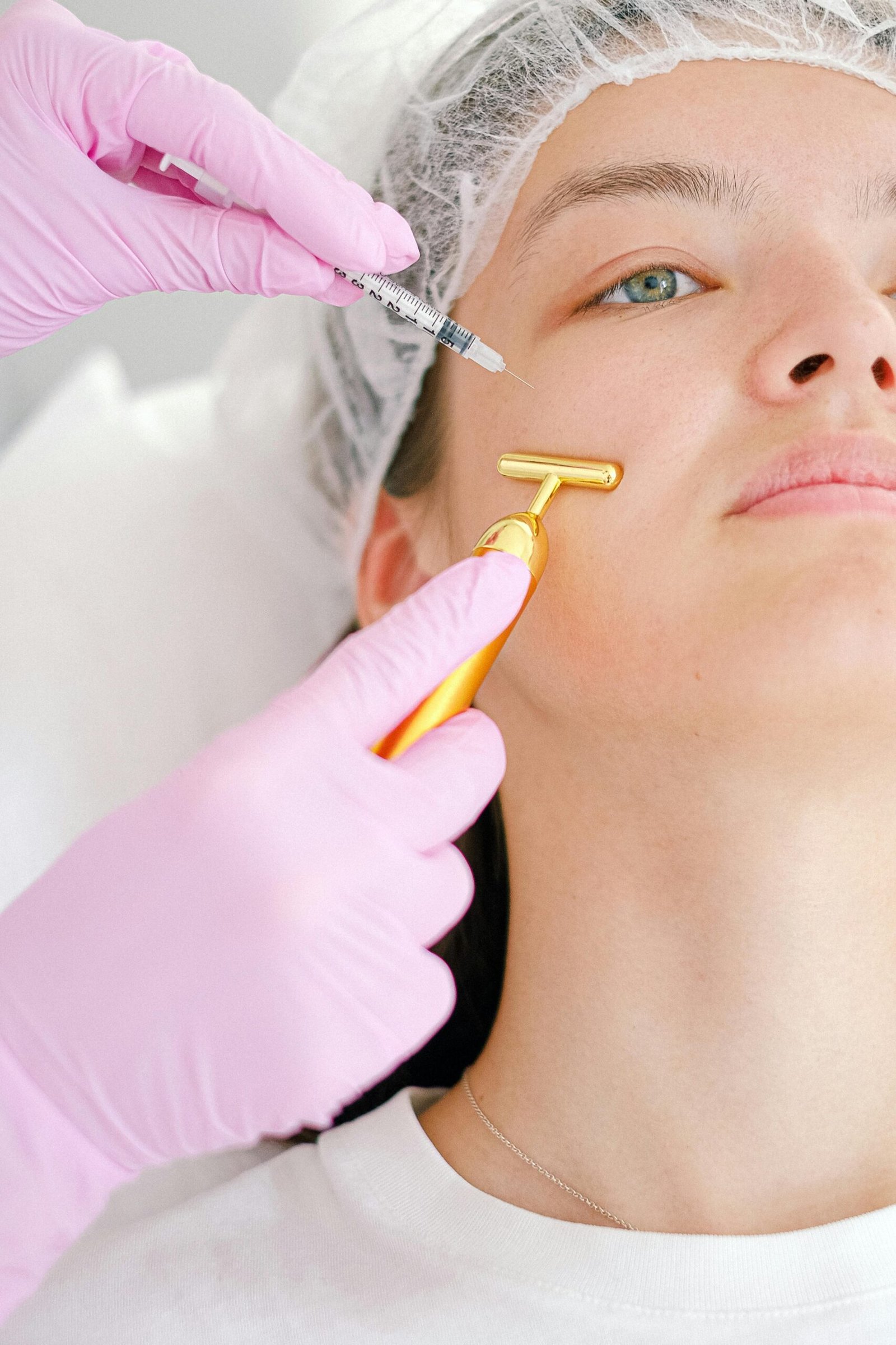 Close-up of a young woman receiving a beauty treatment involving a syringe and face roller at a clinic.