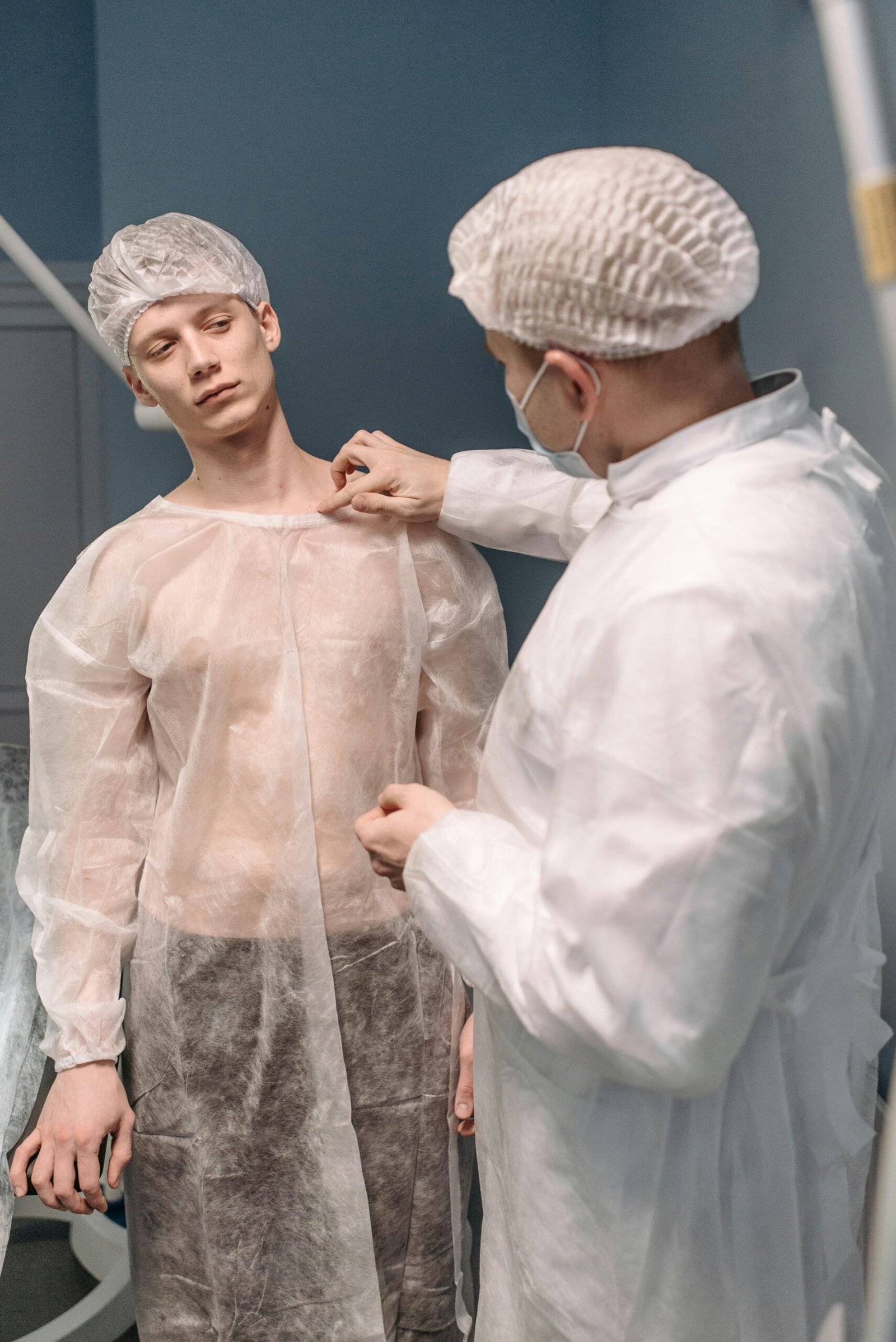 A doctor examines a patient in a medical clinic wearing gowns and hair nets, focusing on healthcare procedures.